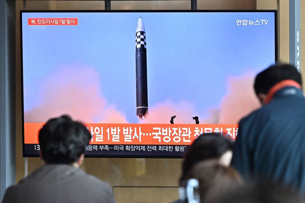 This file picture taken on May 4, 2022 shows people watching a television screen showing a news broadcast with file footage of a North Korean missile test, at a railway station in Seoul. ― AFP pic