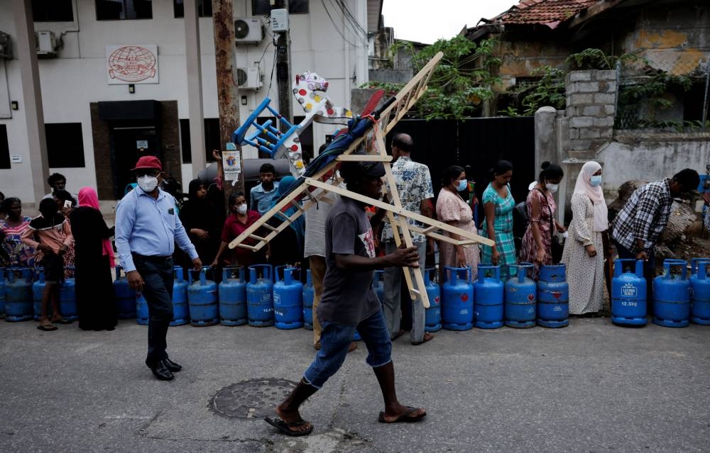 A man walks down a road as people wait in a line to buy domestic gas tanks near a distributor, amid the country's economic crisis, in Colombo, Sri Lanka May 24, 2022. ― Reuters pic