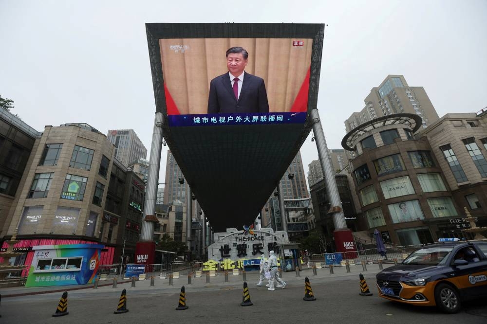 Medical workers in protective suits walks past a giant screen showing Chinese President Xi Jinping at an event celebrating the 100th anniversary of the founding of the Chinese Communist Youth League, amid the Covid-19 outbreak in Beijing May 10, 2022. — Reuters pic