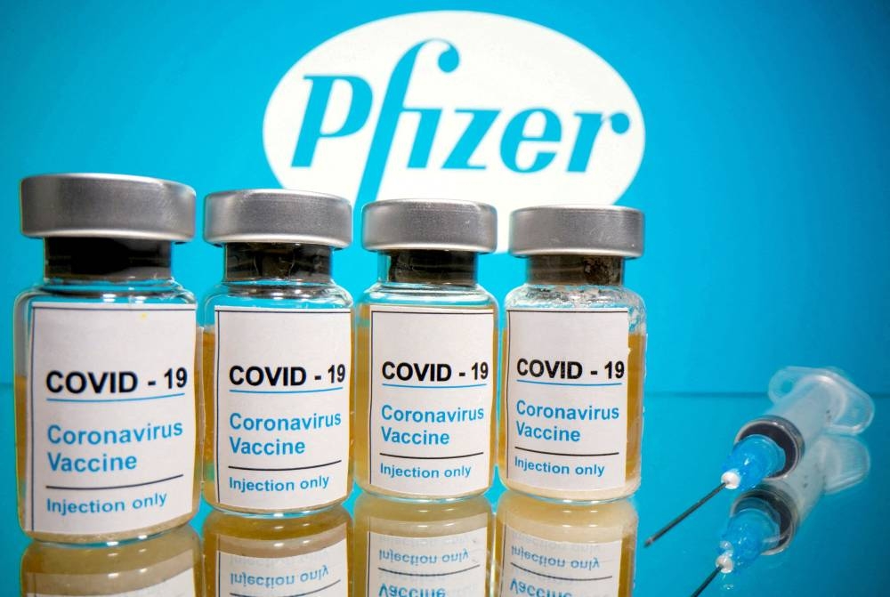 Vials with a sticker reading, ‘Covid-19 / Coronavirus vaccine / Injection only’ and a medical syringe are seen in front of a displayed Pfizer logo in this illustration taken October 31, 2020. — Reuters pic