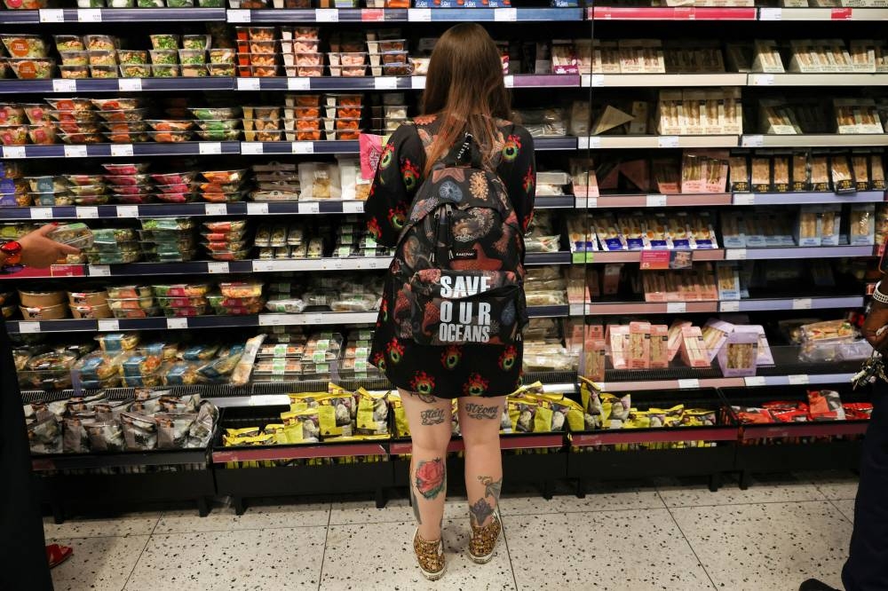 A person wearing a backpack with the slogan ‘Save our oceans’, looks at food goods in a shop as UK inflation heads towards 10 per cent in London June 16, 2022. — Reuters pic