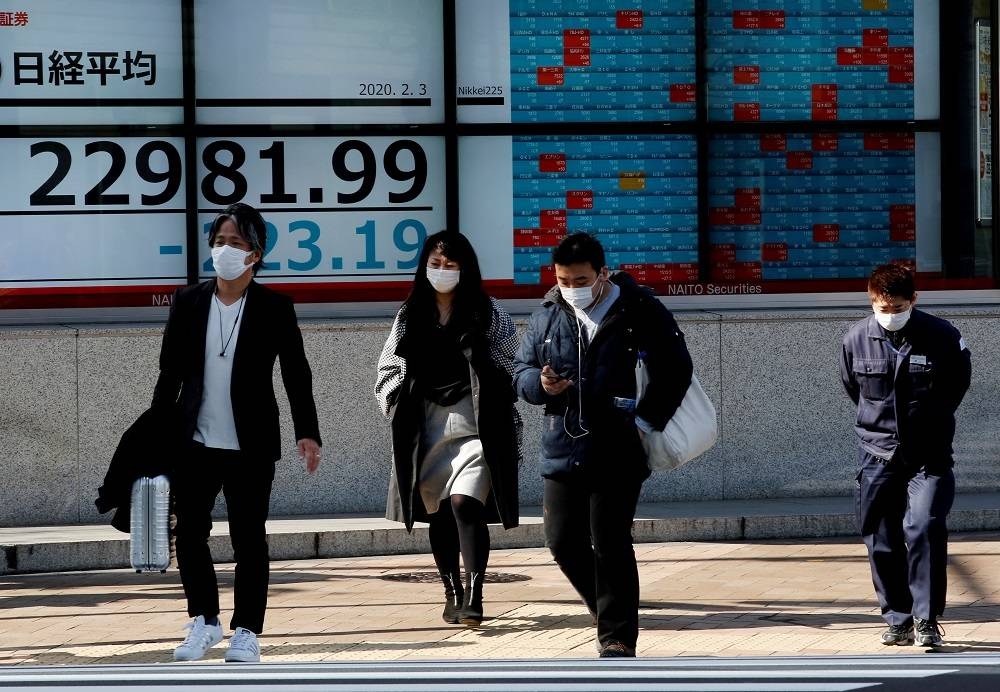 People wearing surgical masks walk past a screen showing Nikkei index outside a brokerage in Tokyo February 3, 2020. — Reuters pic