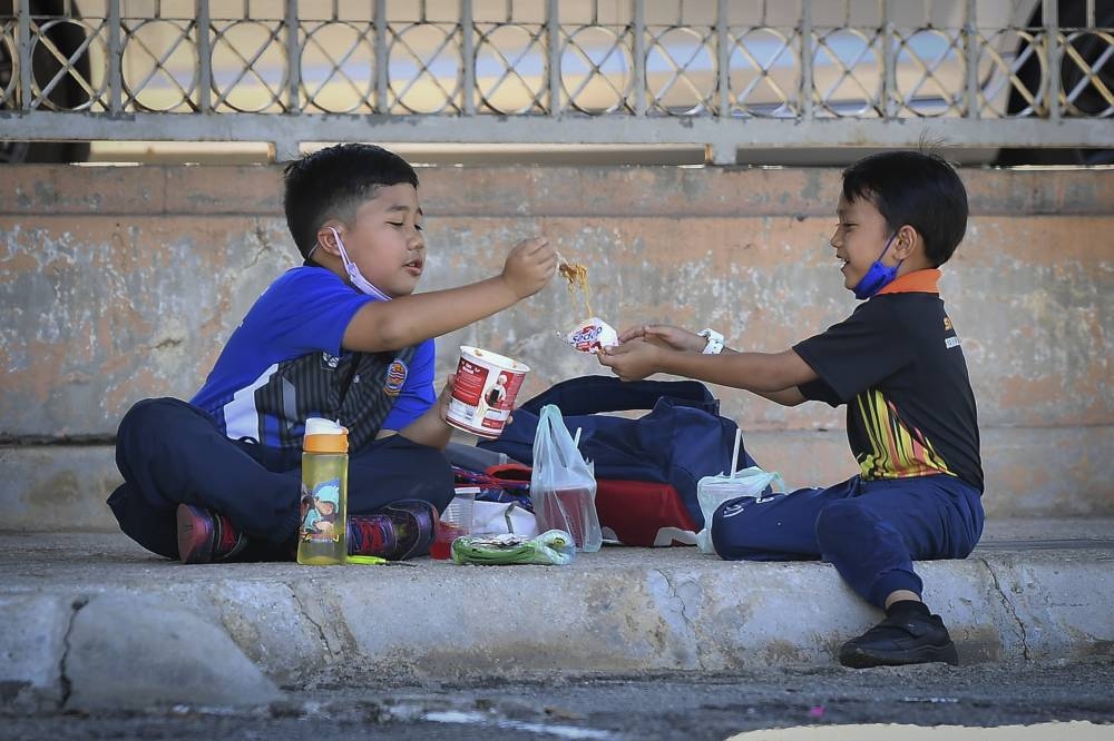 These two children were seen sharing food after the school session in Precinct 9 in Putrajaya, June 27, 2022. Health Minister Khairy Jamaluddin said the protracted Covid-19 outbreak situation and the economic impact on the people were expected to increase the trend of nutritional problems among children, especially those from low-income families. — Bernama pic 