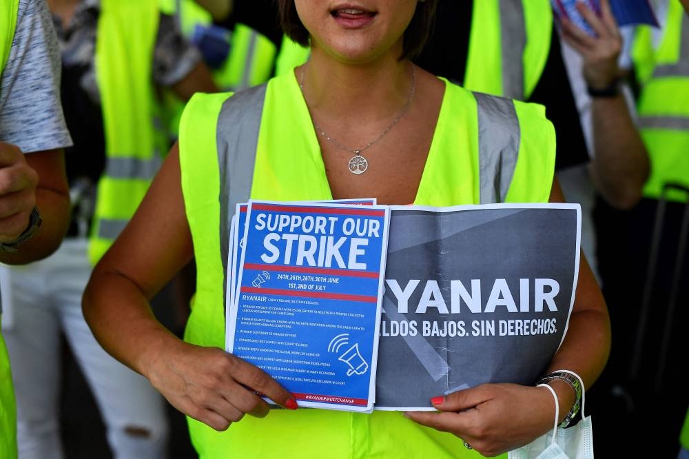 A Ryanair employee holds flyers reading ‘Support our strike’ as they protest at the Terminal 2 of El Prat airport in Barcelona on July 1, 2022. ― AFP pic