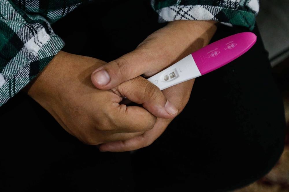 A woman pictured looking at a pregnancy test kit showing a positive result. — Picture by Sayuti Zainudin