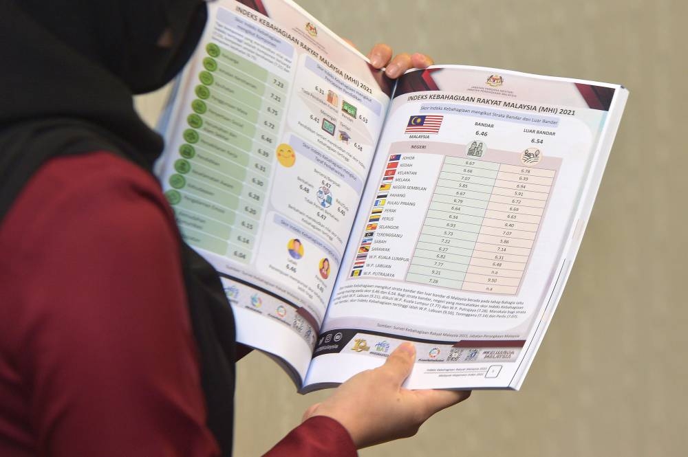 A woman holds up a copy of the report detailing DoSM's Malaysia Happiness Index in Putrajaya July 22, 2022. — Picture by Shafwan Zaidon