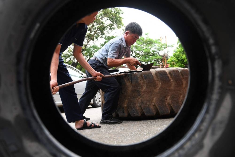 This photo taken on July 8, 2022 shows workers cutting apart a rubber truck tyre outside a workshop in Hanoi. — AFP pic