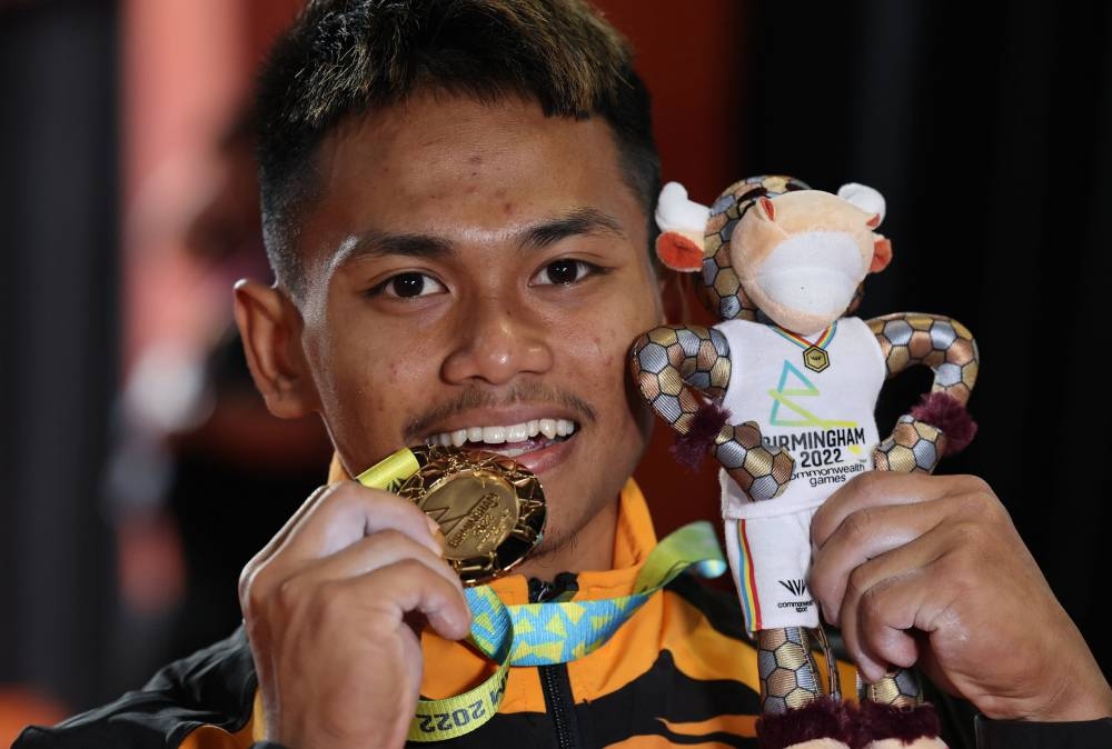 National weightlifter Mohamad Aniq Kasdan shows off the country's first gold medal won in the 55kg category at the Birmingham 2022 Commonwealth Games, July 30, 2022. — Bernama pic