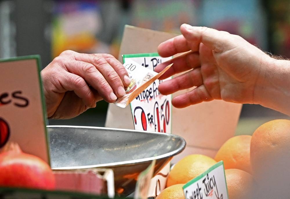 In this file photo taken on May 12, 2022 a customer pays for his fruit and vegetables with a ten pound sterling note, at a trader's market stall in London. — AFP pic