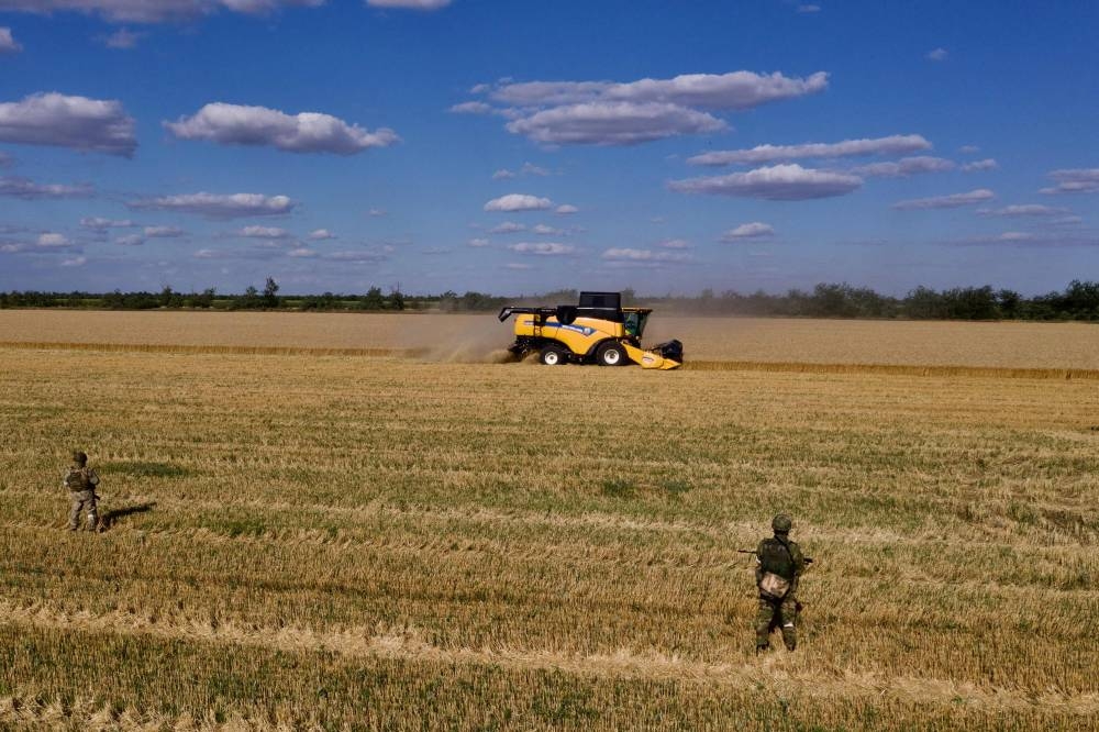 In this aerial picture taken on July 14, 2022 Russian servicemen stand guard in a field as farmers harvest wheat near Melitopol, Zaporizhzhia region, amid the ongoing Russian military action in Ukraine. — AFP pic