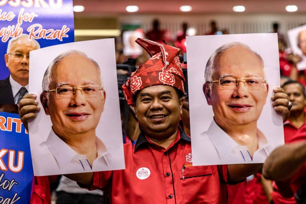 A man holds up pictures of former prime minister Datuk Seri Najib Razak during the Umno special briefing with divisional committee members and leaders at the party's headquarters at the Kuala Lumpur World Trade Centre August 27, 2022. — Picture by Firdaus Latif