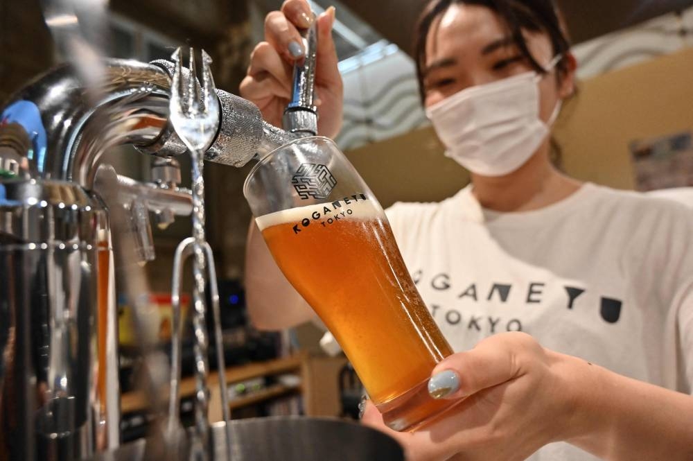 This photo taken on August 13, 2022 shows an employee pouring a craft beer at the entrance to Koganeyu, which is a 