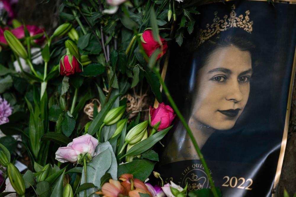 A portrait of Britain's Queen Elizabeth II is seen next to flowers placed outside of Buckingham Palace in London on September 11, 2022. — AFP pic