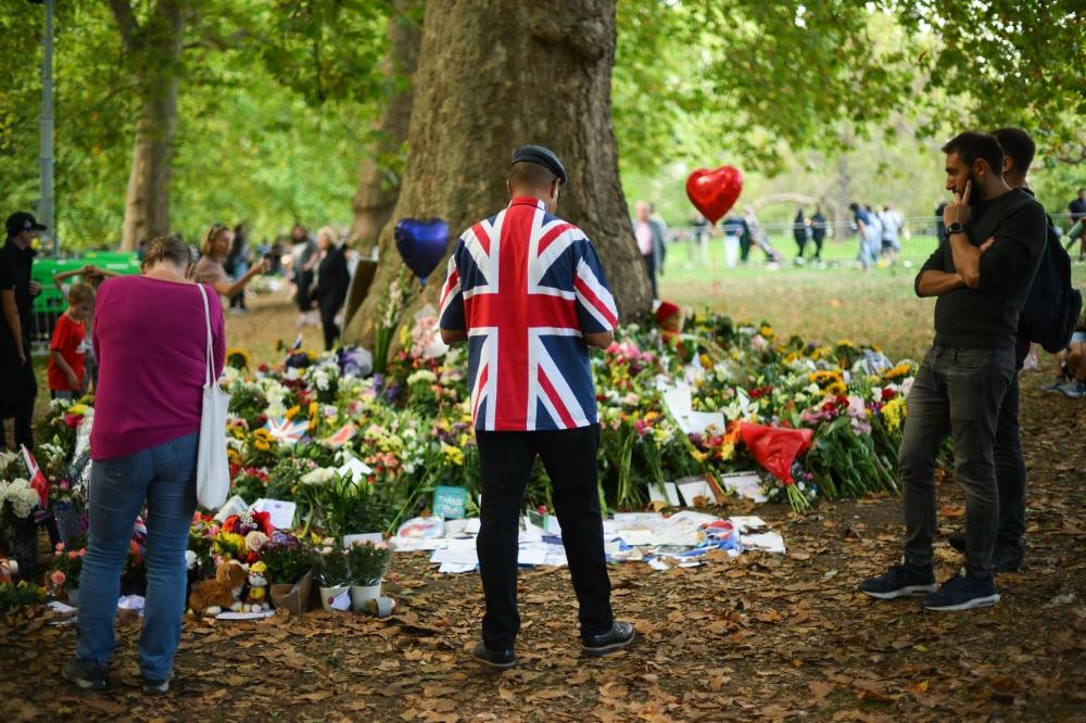 A man wearing a jacket with the Britain national flag on looks at flowers placed by well-wishers in remembrance of Britain's Queen Elizabeth II in Green Park near Buckingham Palace in London on September 11, 2022. — AFP pic