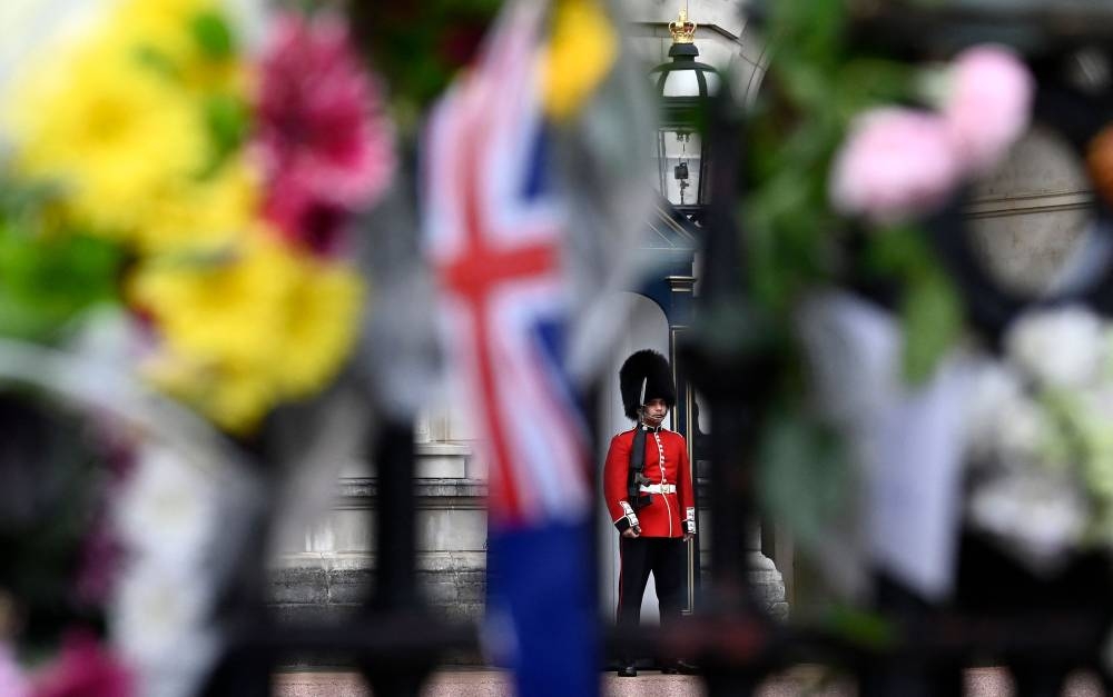 A soldier from the Coldstream Guards is pictured beyond flowers left on the gates of Buckingham Palace, as he stands on duty in London on September 12, 2022, following the death of Queen Elizabeth II on September 8. — AFP pic