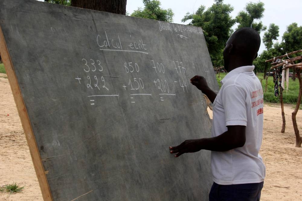 Teacher Leonard Gamaigue writes on a board as he teaches elementary arithmetic during his class at an open-air classroom as part of his mobile school program offering a rare chance of education for their nomadic community, at a nomad camp in Toukra, outside N'Djamena, Chad, September 1, 2022. — Reuters pic