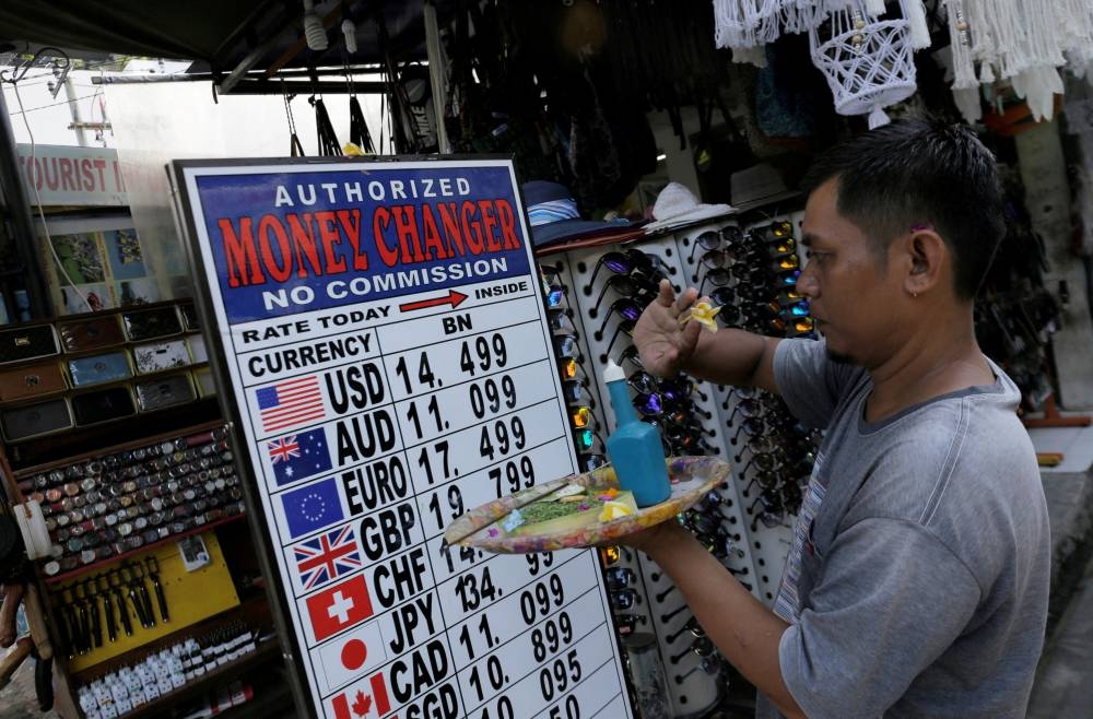 A Balinese man makes a Hindu offering outside a shop which offers currency exchange services in Kuta, on the resort island of Bali, Indonesia  April 30, 2018. — Reuters pic