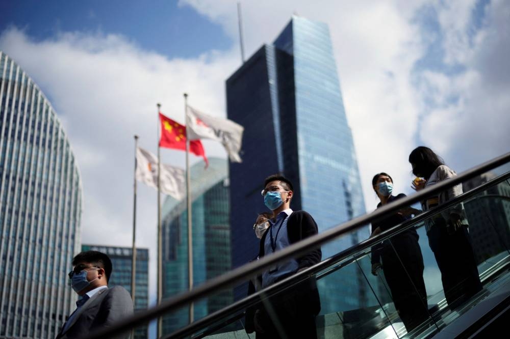 People wearing face masks following the coronavirus disease (COVID-19) outbreak ride an escalator past office towers in the Lujiazui financial district of Shanghai October 17, 2022. — Reuters pic