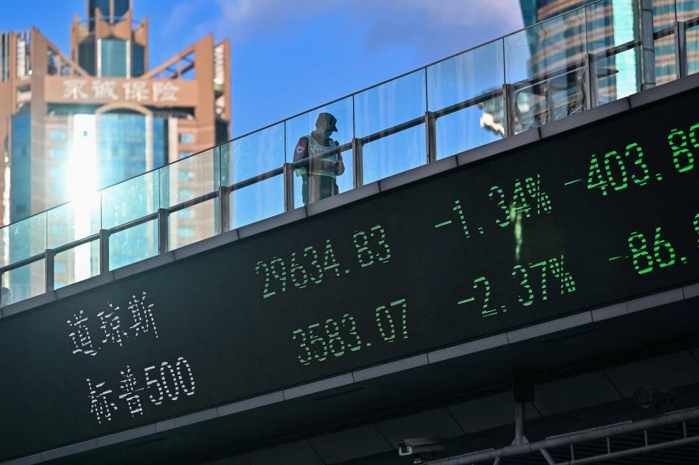 A guard walks across a bridge with a stocks indicator board in the financial district of Lujiazui in Shanghai on October 17, 2022. — AFP pic