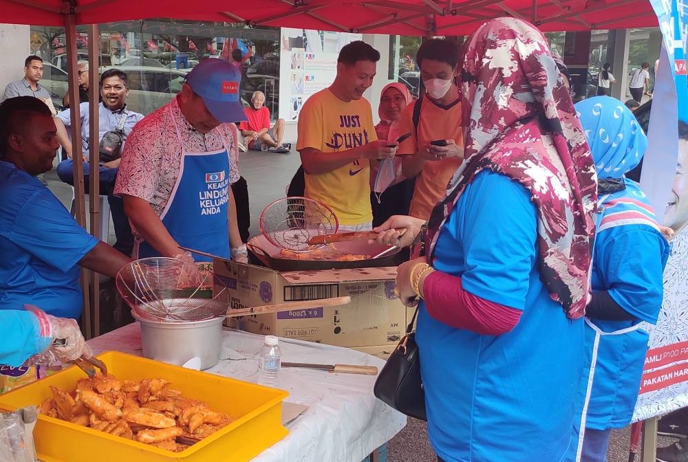 PKR deputy president Pandan Rafizi Ramli (wearing apron) cooks banana fritters while on the campaign trail in Pandan on November 5, 2022. — Picture by Kenneth Tee