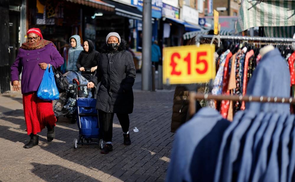 In this file photo taken on February 04, 2022 Shoppers walks past a clothing stall at a market in Walthamstow, east London. — AFP pic