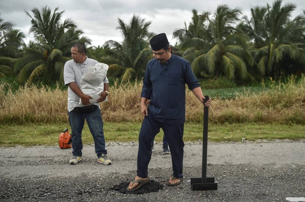 Azlan Sani Zawawi (right), filling asphalt mix into a pothole on a road in Tanjong Karang November 11, 2022. — AFP pic