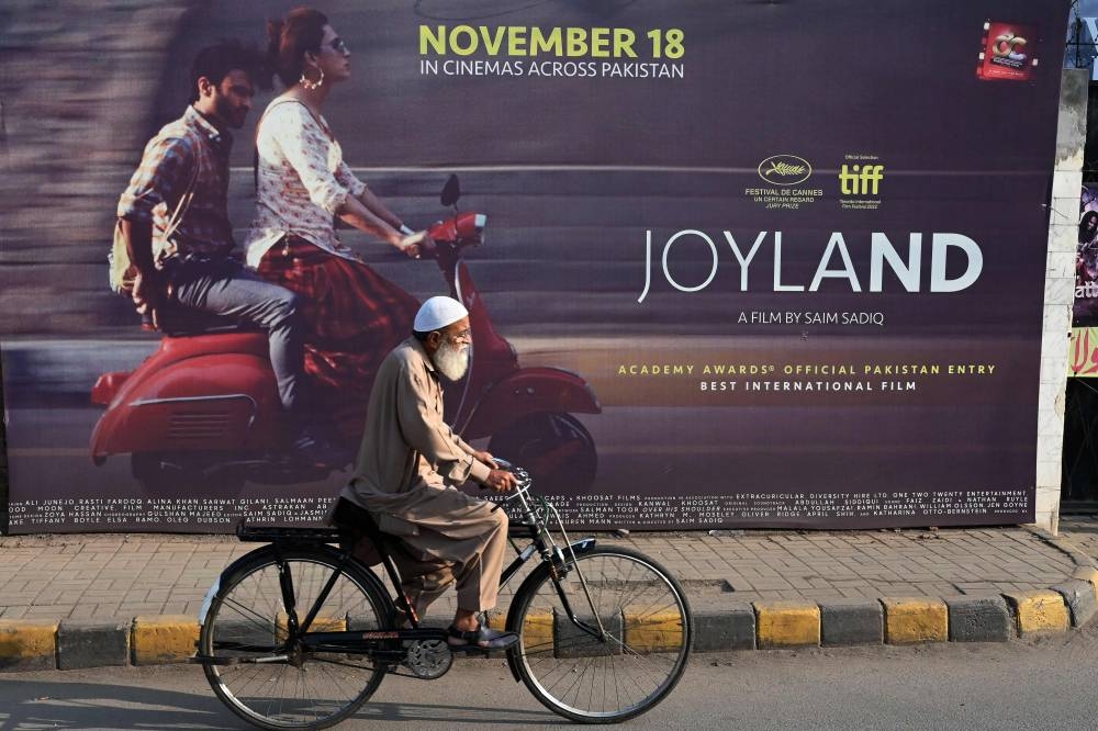 A cyclist rides past a promotional hoarding banner of Pakistan-produced movie 