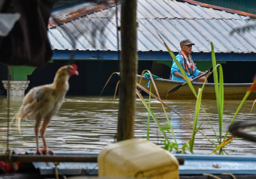 A flood victim uses a boat during the floods at Kampung Tersang, Rantau Panjang in Pasir Mas December 13, 2022. — Bernama pic