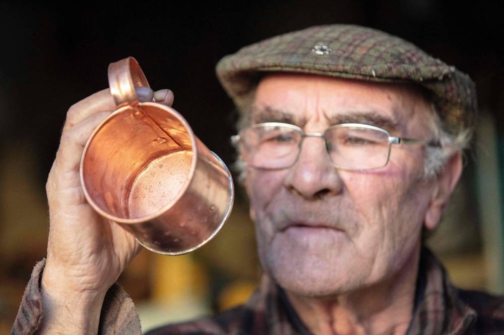 Warmed by a wood burning stove and thinking of the past, James Collins often works with tin late into the evening, the passing of time punctuated by the steady tap of his hammer. — AFP pic