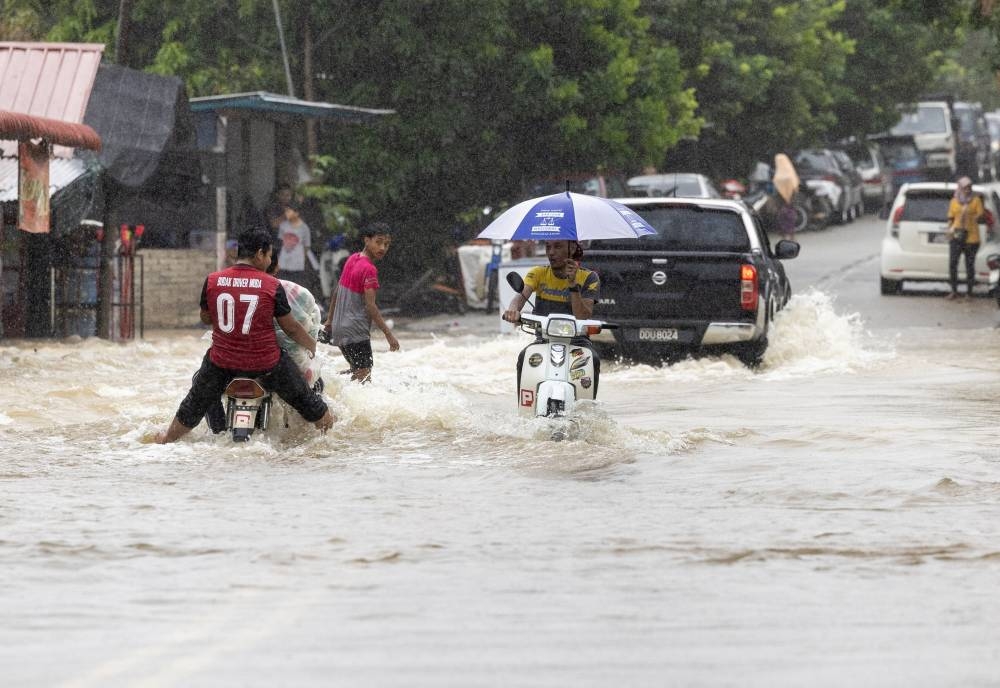 Several vehicles are pictured driving through the flooded road following heavy rain in Kampung Kubang Kual, Rantau Panjang, in Pasir Mas, December 18, 2022. — Bernama pic