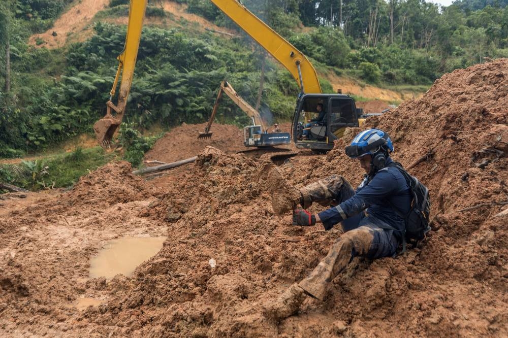 A rescue personnel cleans mud from his shoe. — Picture by Shafwan Zaidon