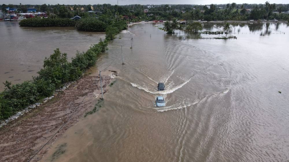 Vehicles drive through the overflowing water of Sungai Golok which began to fill Jalan Pengkalan Kubor to Kampung Simpangan in Tumpat, Kelantan, December 21, 2022. — Bernama pic  