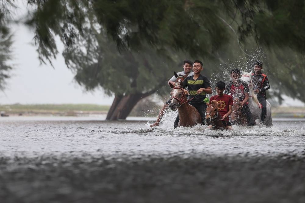 A group of teenagers ride horses in a rain-clogged area in Pantai Teluk Ketapang in Kuala Terengganu, December 21, 2022. — Bernama pic 