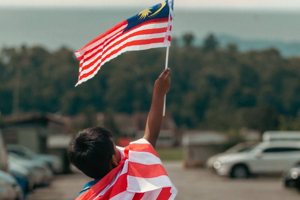 A boy waves the national flag in a park at Cheras August 10, 2022. Pemadam has urged the government to review and study the National Child Protection Policy in an effort to protect the the group. — Picture by Devan Manuel