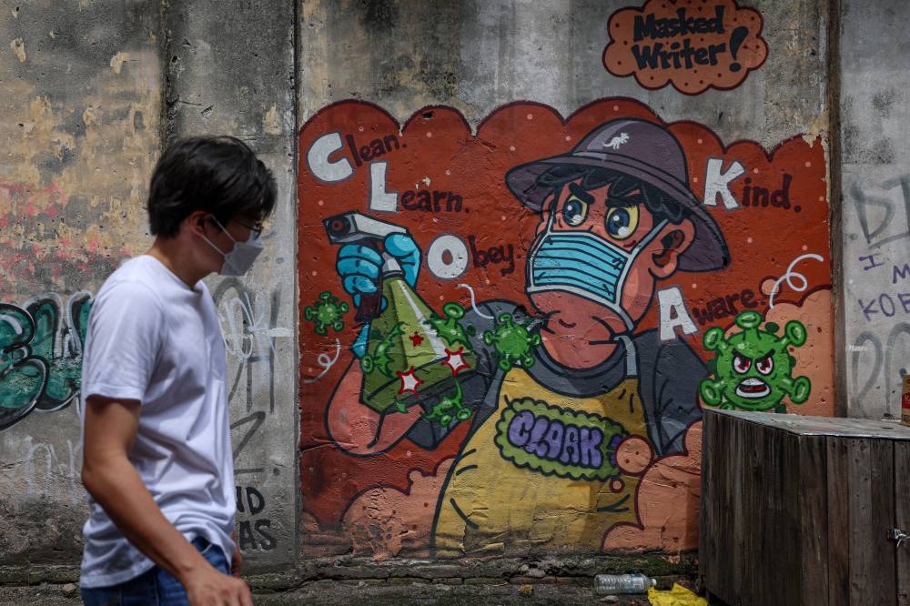 A man wearing a face mask walks past a mural on Jalan Petaling, Kuala Lumpur January 8, 2023. — Bernama pic