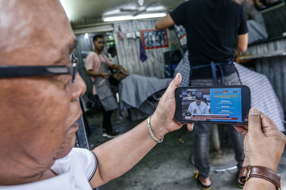 A man watching on his mobile phone as Malaysian Prime Minister Datuk Seri Anwar Ibrahim presented Budget 2023 in Parliament, Kuala Lumpur February 24, 2023.  — Picture by Hari Anggara