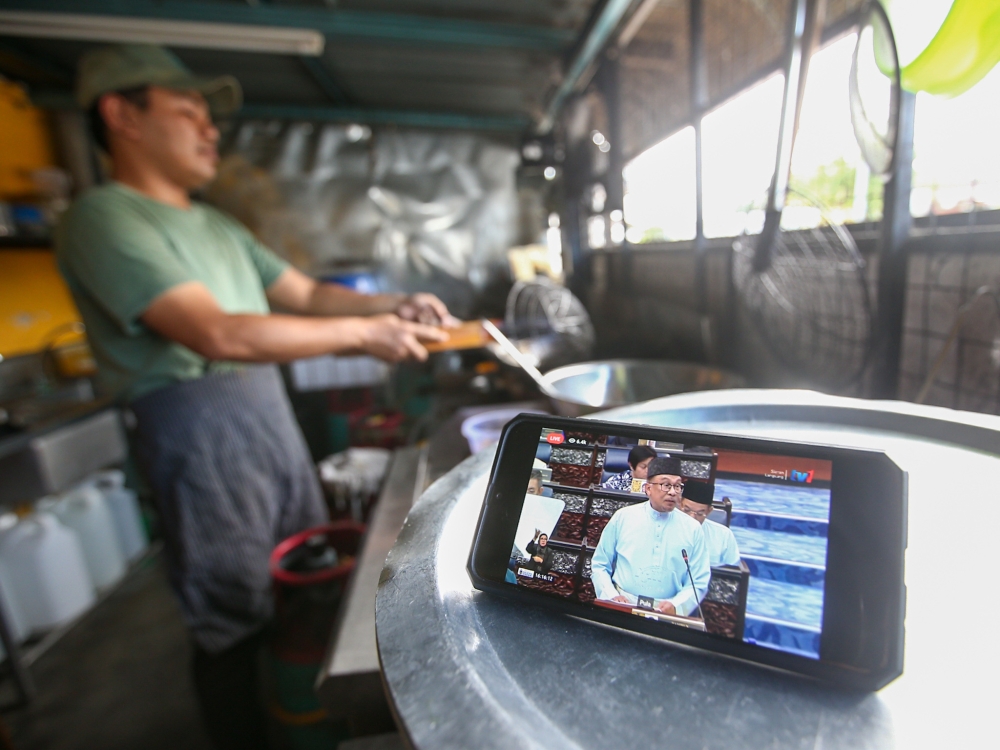 Ahmad Muzakkir Ahmad Zabri, 30, who owns the Ayam Goreng Kunyit Bonggol Sg Rokam in Perak, watces the live feed of Budget 2023 via their smart phones, tabled by the Prime Minister Datuk Seri Anwar Ibrahim February 24, 2023. —  Picture by Farhan Najib