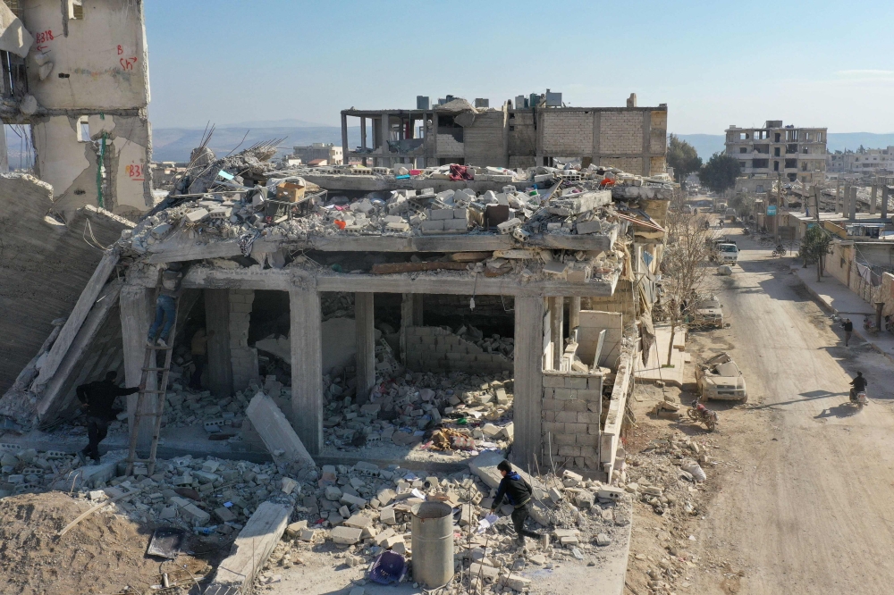 An aerial view shows people trying to recover items from the rubble of a collapsed building in the Syrian rebel-held town of Jindayris on February 15, 2023, following the February 6 earthquake that hit Turkey and Syria. — AFP pic