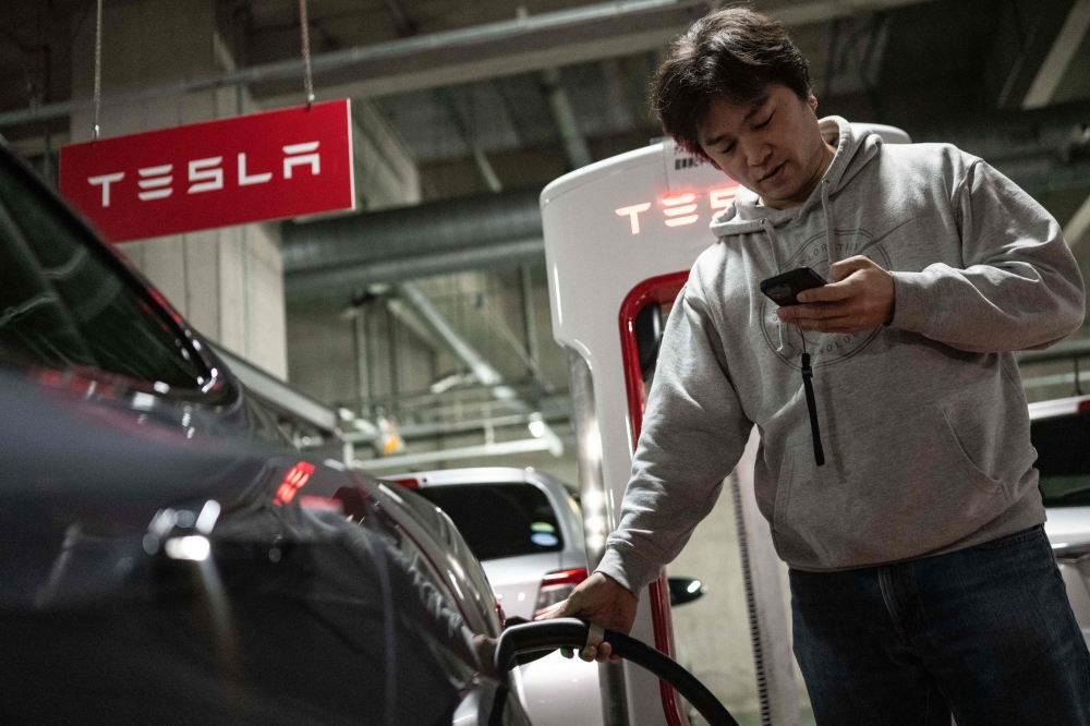 Atsushi Ikeda, the founder and vice president of a Japanese club for Tesla owners, charges his Tesla Model S at a charging station in Tokyo. — AFP pic