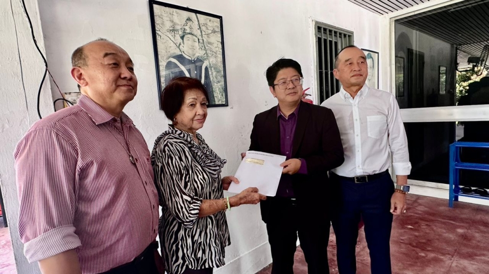 Ewon Benedick (second right) hands over a copy of the ‘Double Six’ crash report to Datin Nancy Mary Mobijohn, widow of Datuk Peter Mojuntin. Also present was Datuk Donald Peter Mojuntin (right) and his brother Charles Peter Mojuntin. — Picture by Julia Chan