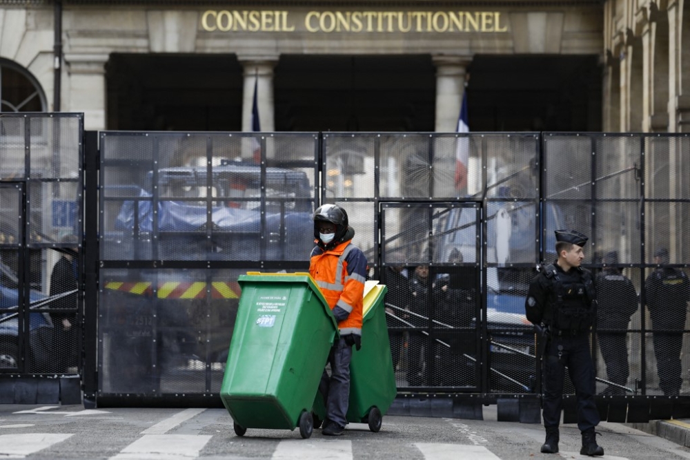 A worker wheels waste containers next to a French gendarme standing guard as a security perimeter is established around France's Conseil Constitutionnel (constitutional council) on the day of a ruling from France's Constitutional Council on a contested pension reform pushed by the French government, in Paris on April 14, 2023. France's top constitutional court is to rule on April 14 on whether to approve the French President's deeply unpopular pensions overhaul after months of protests. — AFP pic