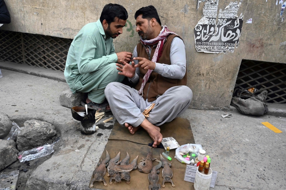 A ‘sanda tael’ balm vendor (right) talks with his customer at his stall in Raja Bazaar in Rawalpindi April 3, 2023. — AFP pic