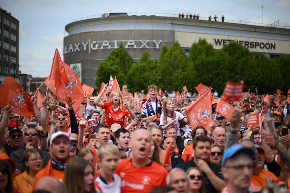 Supporters hold up placards and flags as they  welcome the bus of Luton Town football club players and staff during a parade through the streets of Luton with the Championship playoff trophy, in Luton, north of London on May 29, 2023, as they celebrate their promotion to the English Premier League. — AFP pic