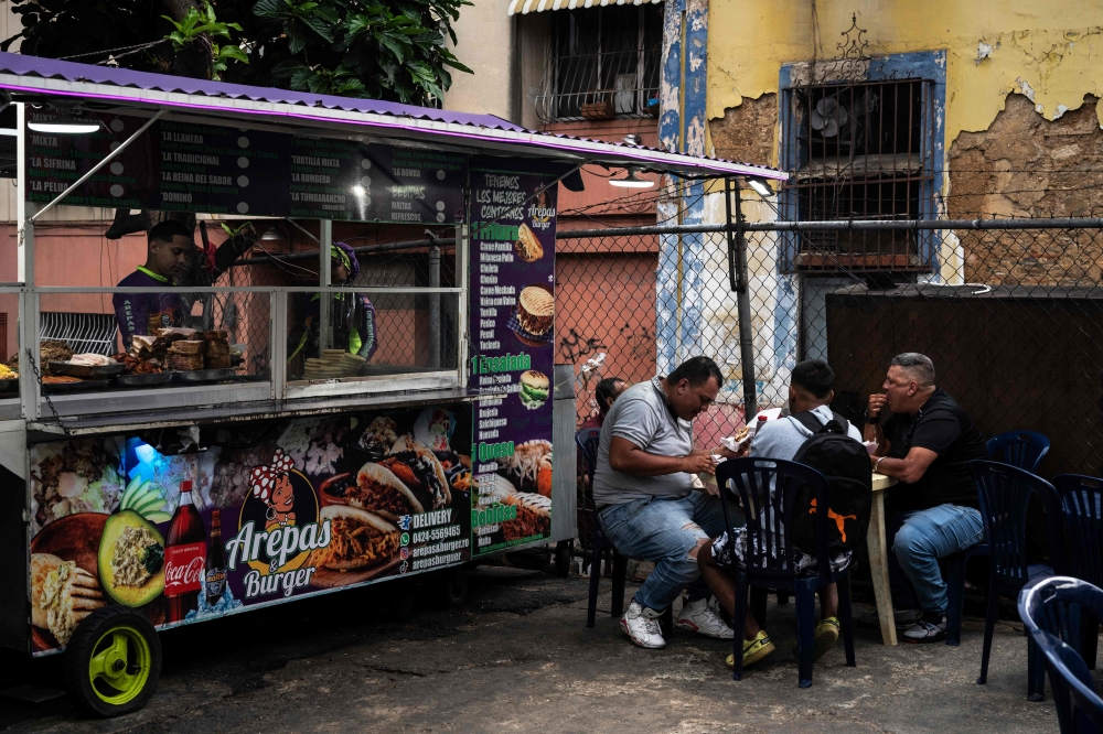 Customers eat the traditional Venezuelan food known as arepas at a food truck parked on a street of the popular neighbourhood of Santa Rosalia, Caracas on May 31, 2023. — AFP pic  