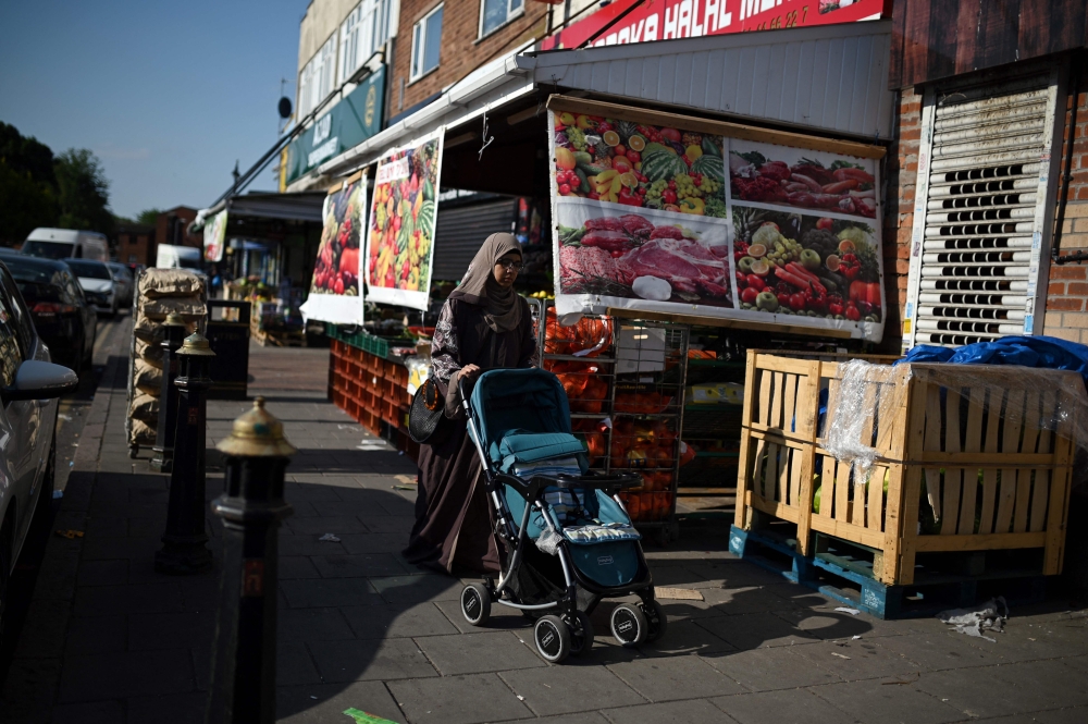 A woman pushing a stroller walks past a food store in the ‘Balti Triangle’ area of Birmingham, central England, on June 7, 2023. — AFP pic