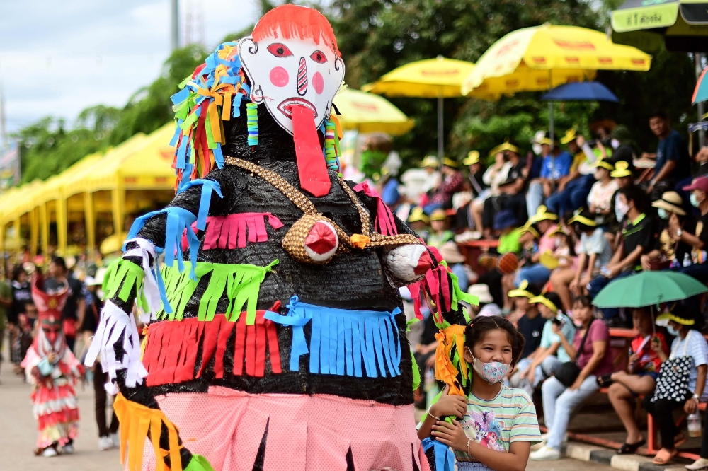 Seorang gadis (kanan) memeluk seorang peserta yang memakai topeng hantu dan kostum berwarna-warni semasa karnival tahunan Phi Ta Khon atau festival hantu di daerah Dan Sai di wilayah Loei, timur laut Thailand pada 24 Jun 2023. — Gambar AFP