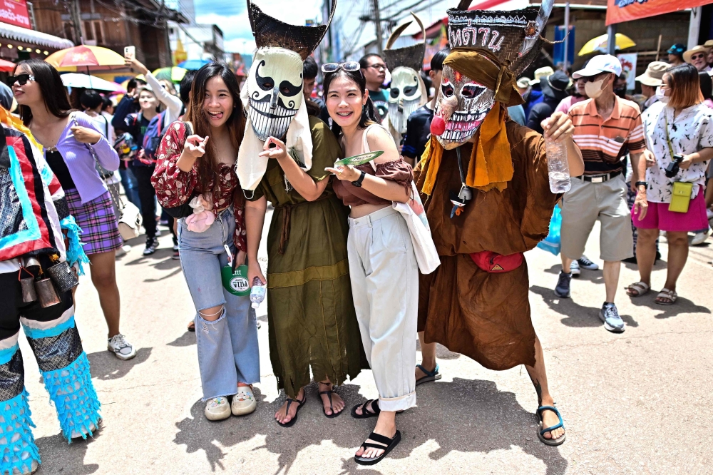 Orang ramai bergambar dengan peserta memakai topeng hantu dan pakaian berwarna-warni semasa perarakan di karnival tahunan atau festival hantu Phi Ta Khon di daerah Dan Sai di timur laut Wilayah Loei Thailand pada 24 Jun 2023. — Gambar AFP