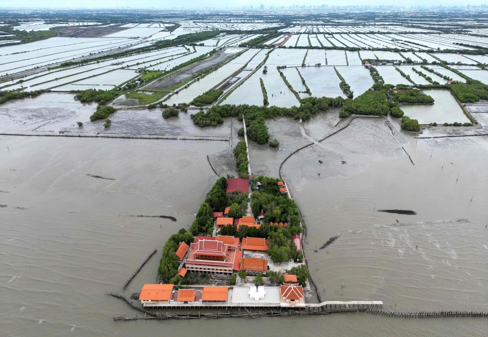 This aerial photograph taken on June 14, 2023 shows a Buddhist temple surrounded by seawater in Ban Khun Samut Chin, a coastal village less than 10km from the edge of Bangkok, as seen in the background. — AFP pic 