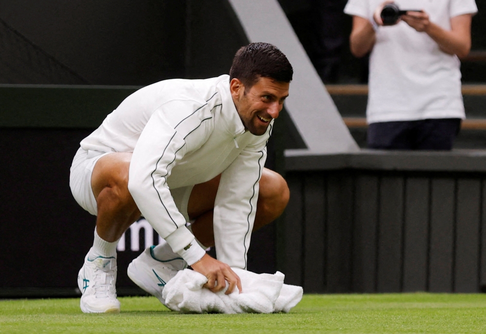 Serbia’s Novak Djokovic wipes the court with a towel as his first round match against Argentina’s Pedro Cachin is suspended due to rain, London, Britain, July 3, 2023. — Reuters pic 