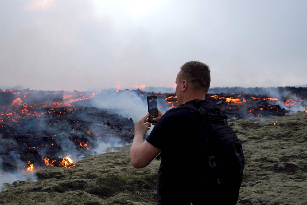 Gambar yang diambil pada 10 Julai 2023 ini menunjukkan seorang lelaki mengambil gambar lava yang mengalir semasa letusan gunung berapi di Litli Hrutur, barat daya Reykjavik di Iceland.  — Gambar AFP
